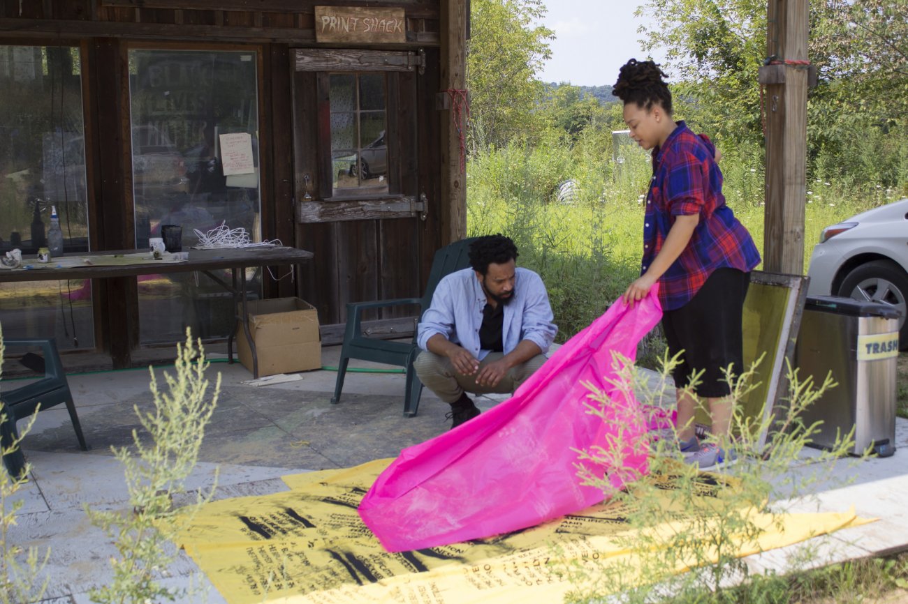 a male and female artist work together outside to prepare cloth for screen printing