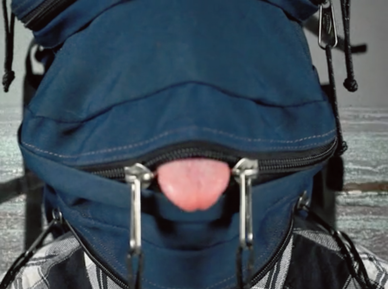 Video still of person wearing navy fabric mask with a slighting unzipped horizontal zipper in the front, the person's tongue is sticking out.