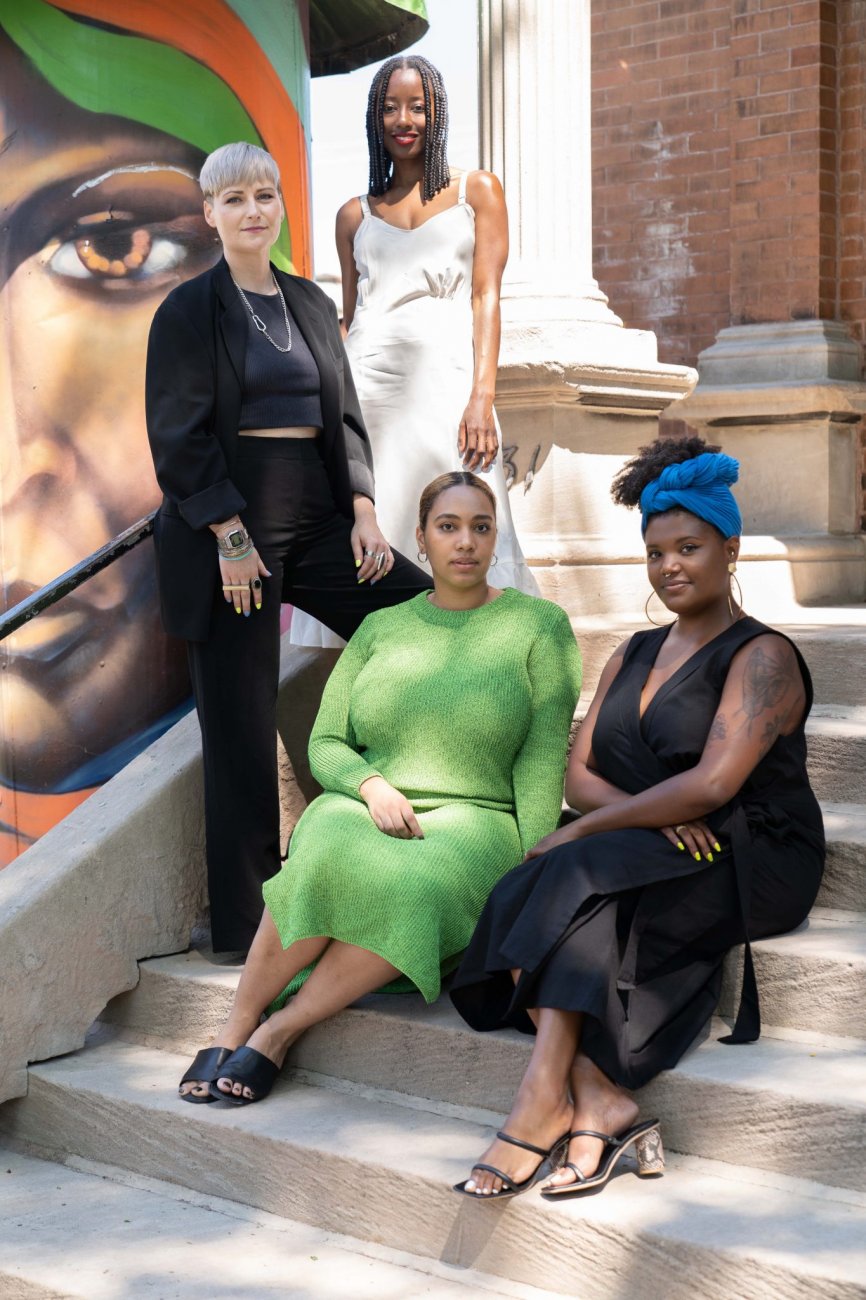 A group of smiling arts organizers pose seated and standing on stone steps