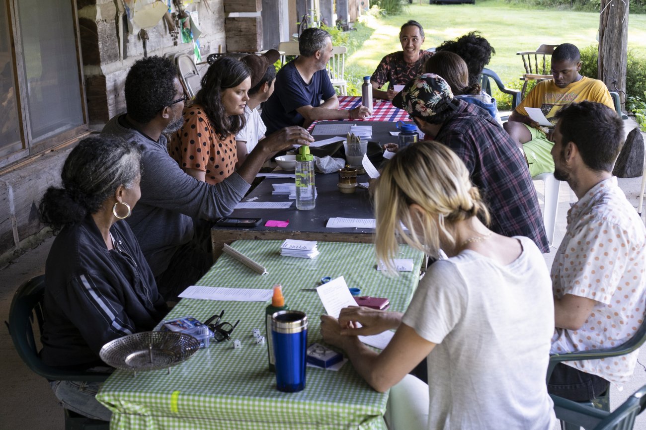 a group of artists gather at a picnic table with papers and other materials