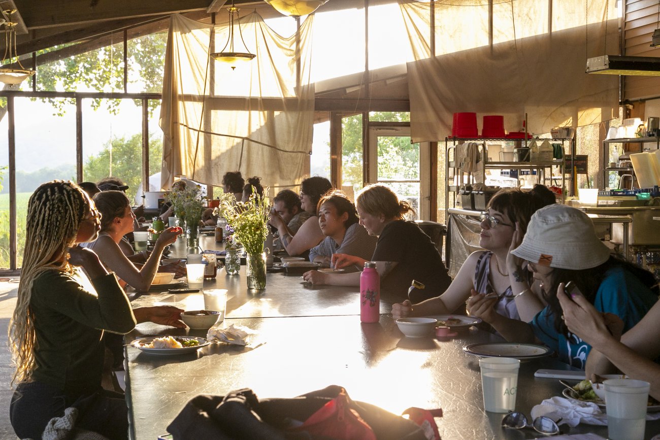 Group of artists seated for dinner lit by the sunset in an indoor/outdoor kitchen