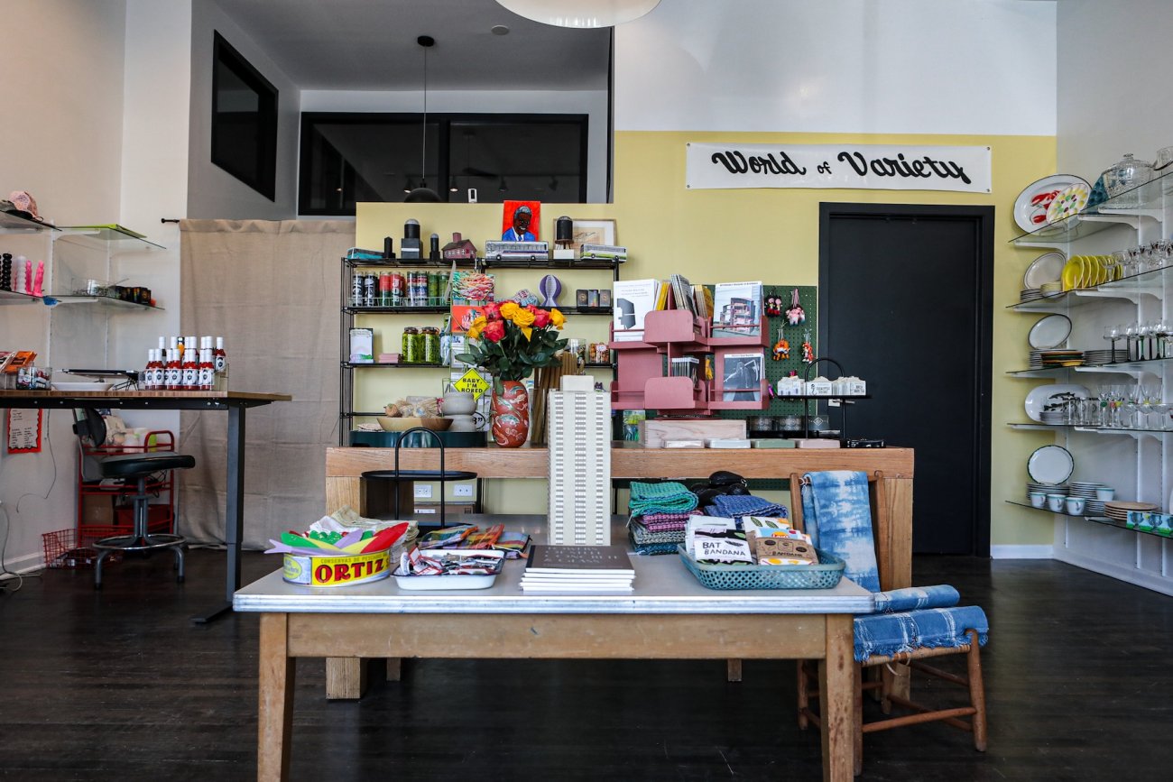 Shop with a variety of objects and artworks on shelves and tables. A sign reading "World of Variety" hangs from the wall in the top right corner of the image.