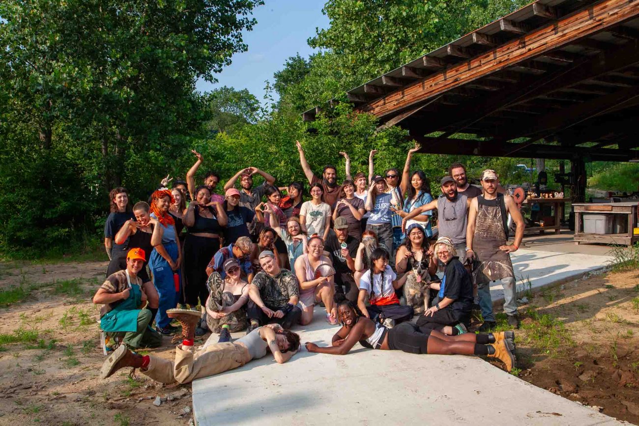 Group of posing and smiling artists in front of trees and large timber roof