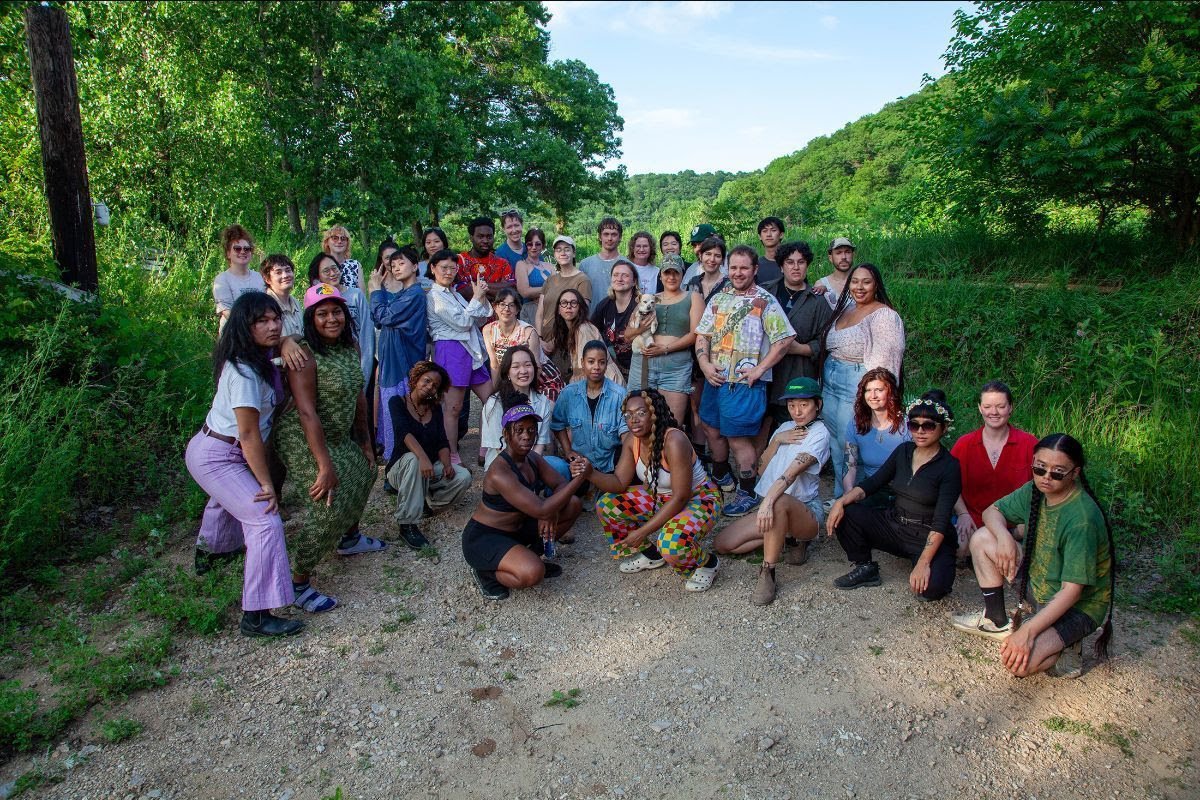 Group shot of artist residents all gathered on a gravel drive surrounded by green landscape