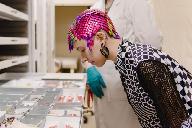 Image of person wearing colorful head dress looking down at pieces of jewelry 