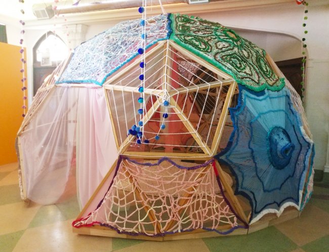 Photograph of geodesic dome covered in a variety of fabrics and crocheted materials.