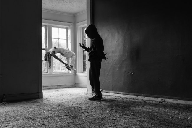 Black and white photography of two figures in a house, one is levitating on their back.