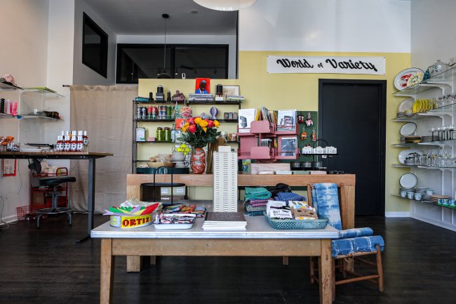 Shop with a variety of objects and artworks on shelves and tables. A sign reading "World of Variety" hangs from the wall in the top right corner of the image.